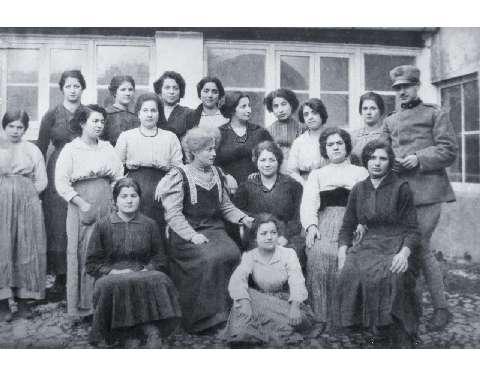 Un gruppo di operaie impiegate nel sacchettificio-tipografia Fratelli Reali. Al centro seduta in posizione di semi-maestà la signora Amalia Reali con un vestito scuro con fregi chiari nel decoltè, 1920-1930