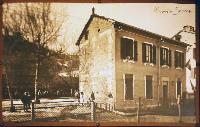 La storica sede della SMS Corale Po e Borgo Po e, a seguire e a tutt'oggi, della Cooperativa Borgo Po e Decoratori. L'edificio venne costruito su un terreno acquistato nel 1909 e venne completato nel 1911. La fotografia viene attribuita con ogni probabilità poco dopo la conclusione dei lavori, come confermerebbero gli abiti dei presenti e l'uso di un apparecchio a banco ottico (correzione delle deformazioni prospettiche)