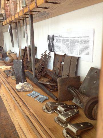 La bacheca con alcuni attrezzi, in primo piano da sn.:  scalpello per tagli metallici, pomice per lucidatura a tampone (inizi Novecento), cerniere per mobili anni cinquanta, dietro vite senza fine per strettoio e serrature per porte interne (fine Ottocento, inizi Novecento)   
