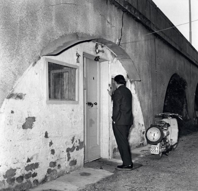 Nel periodo compreso tra il 1945 e il 1949 molta popolazione viveva in estrema povertà derivata da situazioni sociali complesse: molti profughi e superstiti dei campi di concentramento erano costretti a vivere in alloggi di fortuna anche sotto i cavalcavia o nelle baracche lasciate dai militari. L’immagine rappresenta uno di questi luoghi, fine anni Quaranta