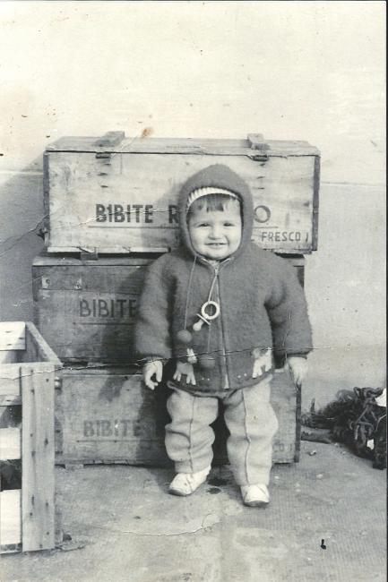 Davide, il figlio di Edda Acquisti e Dario Bartolomei nella vecchia sede in Via Romita 18 a Forlimpopoli posa davanti alle casse di legno contenenti le bibite, 1965