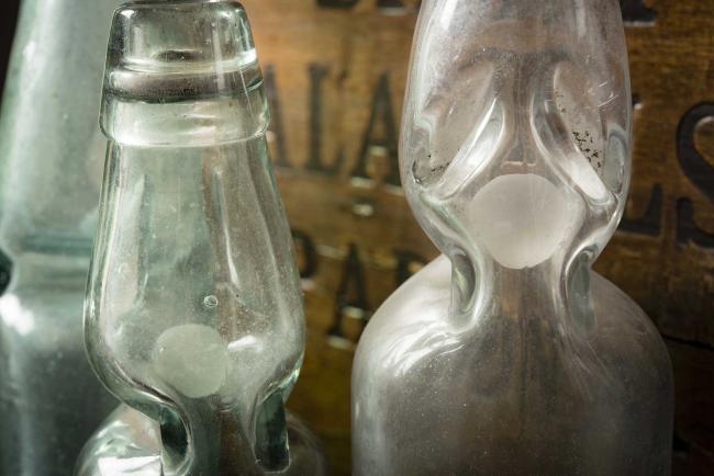 Particolare di bottiglie Codd usate fino agli anni Sessanta per le bevande gassate. All’interno era presente una biglia di vetro che serviva da chiusura ermetica; la pressione interna della bevanda gassata spingeva la biglia contro una guarnizione in gomma nel collo della bottiglia, sigillandola. Per aprirla, bisognava spingere la biglia verso il basso, facendola cadere in un incavo apposito nel vetro dove si fermava durante il consumo, per non ostruire il passaggio del liquido